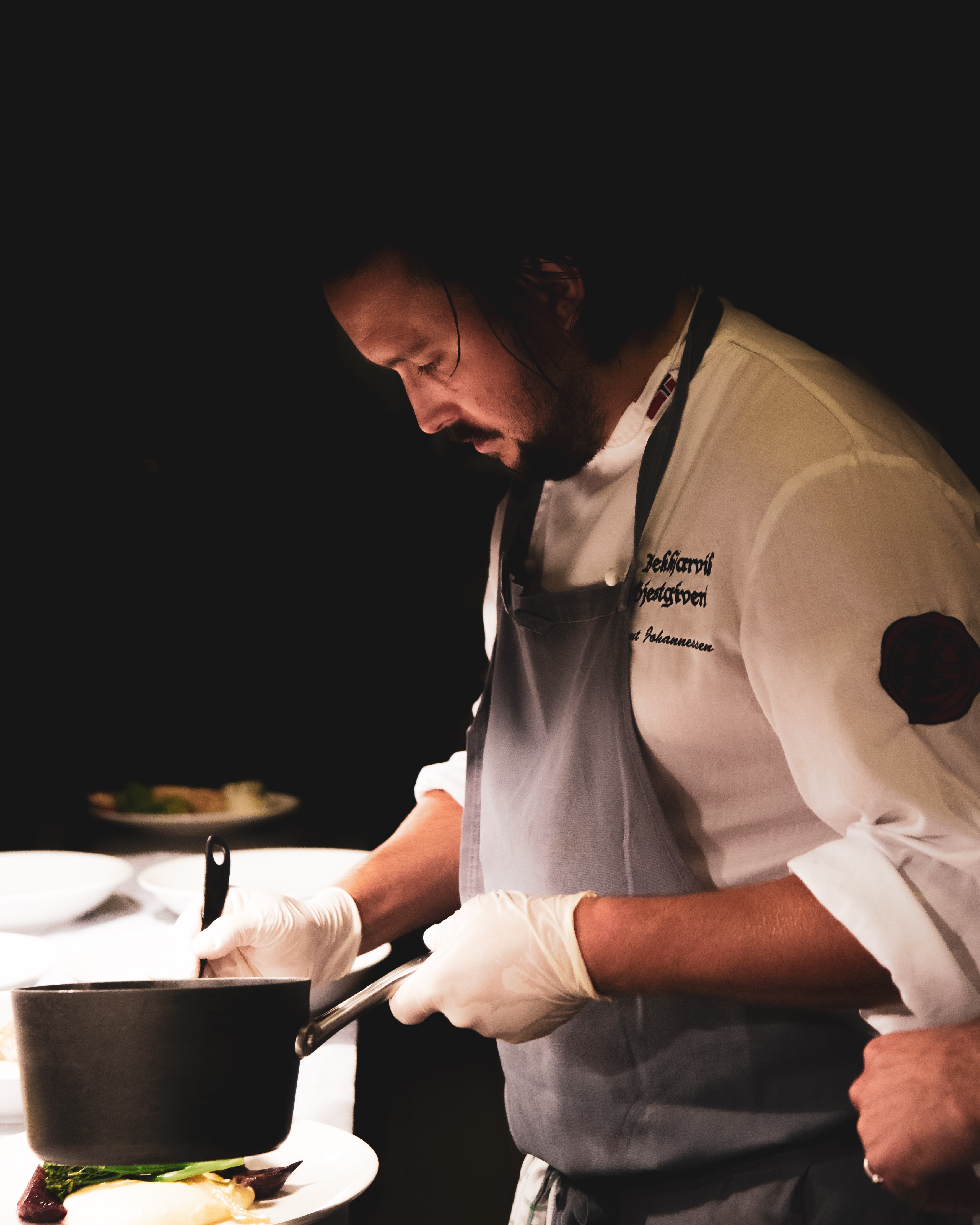 An image capturing a chef on a white uniform and black apron on a dark room